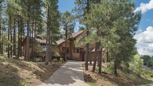 A two-story lodge with a central entrance, surrounded by tall pine trees, and a clear sky. - Burning Tree Lodge - Forest Views, Fire Pit, AC | Pet and Family Friendly (Flagstaff)