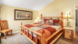 Un dormitorio con una cama de madera, una mesita de noche, una silla, una lámpara y un cuadro en la pared.