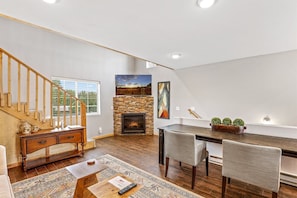 Cozy living area with a stone fireplace, wooden staircase, and modern TV.