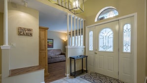 A foyer with a wooden staircase, a bench, a door with stained glass, and a rug.