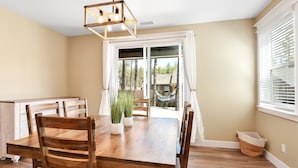 Un comedor con mesa y sillas de madera, una lámpara colgante y vistas al exterior a través de un ventanal corredero.