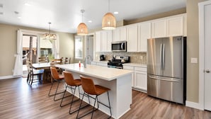 Una cocina moderna con armarios blancos, un refrigerador de acero inoxidable, un microondas y una isla central con taburetes de bar.