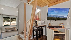 A cozy room with a fireplace, a TV mounted on the wall, and a window overlooking a forested area.