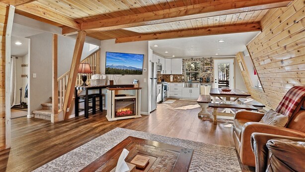 A spacious living area with a wooden ceiling, a fireplace, a kitchen with white cabinets, and a dining area with a table and chairs.