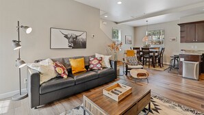 Una sala de estar moderna con un sofá de cuero oscuro, una mesa de centro de madera y un comedor con una mesa y sillas de madera.