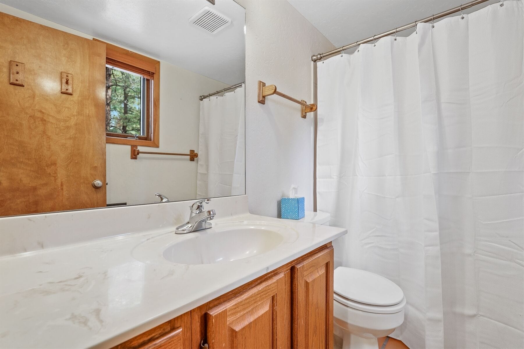 A bathroom with a white sink, wooden cabinets, a mirror, a toilet, and a shower curtain.