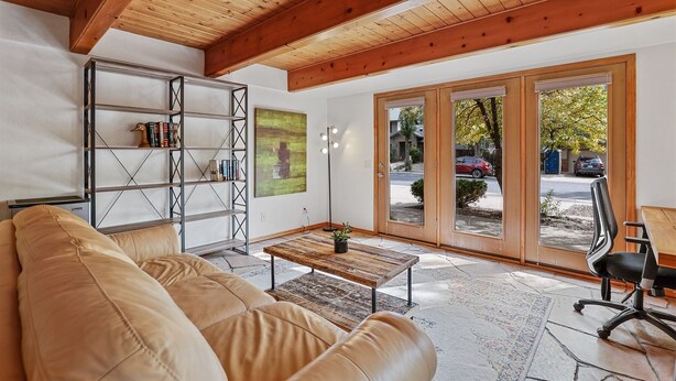 A living room with a leather sofa, a wooden coffee table, a metal bookshelf, and a large window with a view of the street. - Hummingbird Haven | Pet-Friendly Casita | Cozy Gas Fireplace | Close to Downtown (Flagstaff)