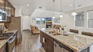A modern kitchen with granite countertops, stainless steel appliances, and a central island with a sink. - Our Happy Place | Minutes to Downtown & NAU | Brand New Home (Flagstaff)