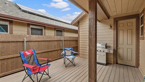 A covered patio with a wooden deck, two folding chairs, a grill, and a door. - Our Happy Place | Minutes to Downtown & NAU | Brand New Home (Flagstaff)