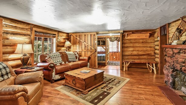 A log cabin interior with a wooden floor, leather furniture, a wooden coffee table, and a staircase leading to a loft. - Rustic Star | Authentic Log Cabin in the Woods | Near the Grand Canyon, Flagstaff & Williams (Bellemont)