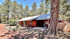 A rustic log cabin with a porch, surrounded by tall trees and a gravel driveway. - Rustic Star | Authentic Log Cabin in the Woods | Near the Grand Canyon, Flagstaff & Williams (Bellemont)