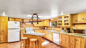 A kitchen with wooden cabinets, a refrigerator, stove, and bar stools. - Rustic Star | Authentic Log Cabin in the Woods | Near the Grand Canyon, Flagstaff & Williams (Bellemont)