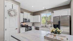 A modern kitchen with white cabinetry, stainless steel appliances, and a marble countertop. - Take Me To The Mountains | Game Room | Fire Pit | Fenced Yard | Dog Friendly (Flagstaff)