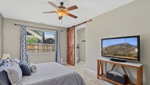 A bedroom with a bed, a ceiling fan, a TV on a wooden stand, and a window with curtains. - Take Me To The Mountains | Game Room | Fire Pit | Fenced Yard | Dog Friendly (Flagstaff)