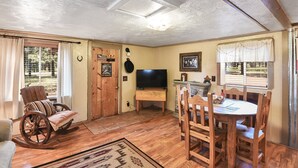 A cozy living room with a wooden rocking chair, a dining table with chairs, a television, and a fireplace.