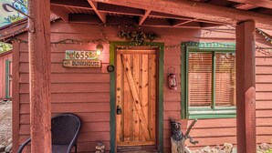 A rustic wooden building with a wooden door, a sign reading "655 The Bunkhouse", and a green window with blinds.