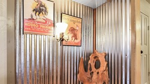 A rustic interior with corrugated metal walls, a vintage poster, a wall-mounted light fixture, and a wooden chair.