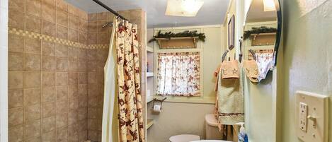 A bathroom with a bathtub, a sink, and a toilet. There is a shower curtain with a pattern, a window with curtains, and a mirror.