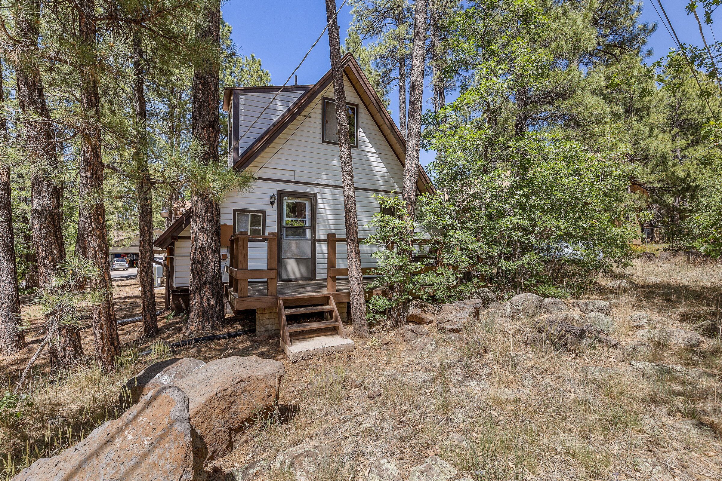 Une cabane dotée d’une terrasse en bois, entourée de grands pins et d’un paysage rocheux.