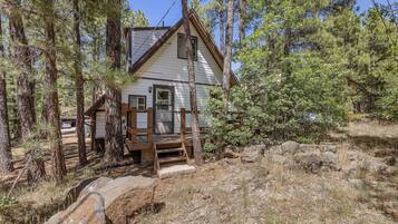 Une cabane dotée d’une terrasse en bois, entourée de grands pins et d’un paysage rocheux.