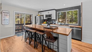 Una cocina moderna con una isla de madera, electrodomésticos de acero inoxidable y amplias ventanas con vistas a un bosque.