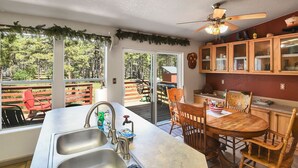 A kitchen with a large island, a dining area with wooden chairs, and a view of a backyard with a wooden deck and chairs.