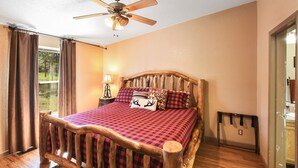 A bedroom with a wooden bed, a ceiling fan, a nightstand with a lamp, and a window with curtains.