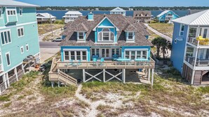 Une maison située en bord de mer, dotée d’une terrasse en bois, de nombreuses fenêtres et offrant une vue sur l’océan.
