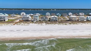 Un quartier résidentiel situé sur la côte, avec des propriétés donnant sur la plage, notamment des maisons dotées de balcons et une plage en premier plan.