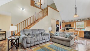A spacious living room with a large gray sectional sofa, a wooden staircase, and a kitchen area in the background. - Canopy Cabin | 3 BR/3 BA with Hot Tub (Townsend)