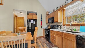 A kitchen with wooden cabinets, a refrigerator, a microwave, and a dishwasher. - Canopy Cabin | 3 BR/3 BA with Hot Tub (Townsend)