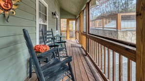 A wooden porch with a stone wall, a wooden railing, and a view of a stone pathway. - Canopy Cabin | 3 BR/3 BA with Hot Tub (Townsend)