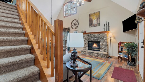 A spacious living room with a stone fireplace, a wooden staircase, and a television mounted on the wall. - Canopy Cabin | 3 BR/3 BA with Hot Tub (Townsend)
