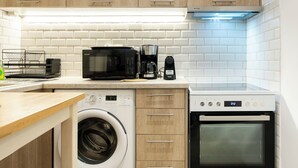 A compact kitchen with wooden cabinets, a washing machine, a microwave, a coffee maker, and an oven.
