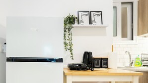 A compact kitchen with a white refrigerator, a small countertop, a coffee machine, and a sink.