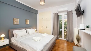 A modern bedroom with a large bed, bedside tables, a flat-screen TV, and a sliding glass door to a balcony.