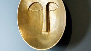 A round, gold-colored object with a face-like design on a plain background.