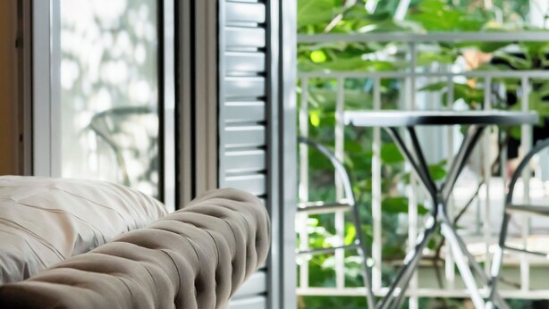 A room with a sofa, a sliding glass door leading to a balcony with a table and chairs.