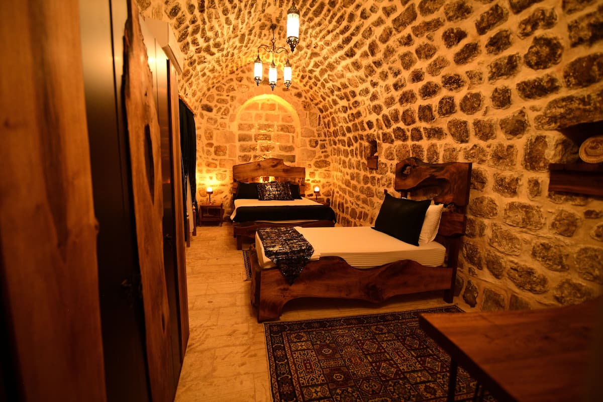 Ein Zimmer mit Steinwänden, zwei Holzbetten, einem Chandelier und einem gemusterten Teppich.
