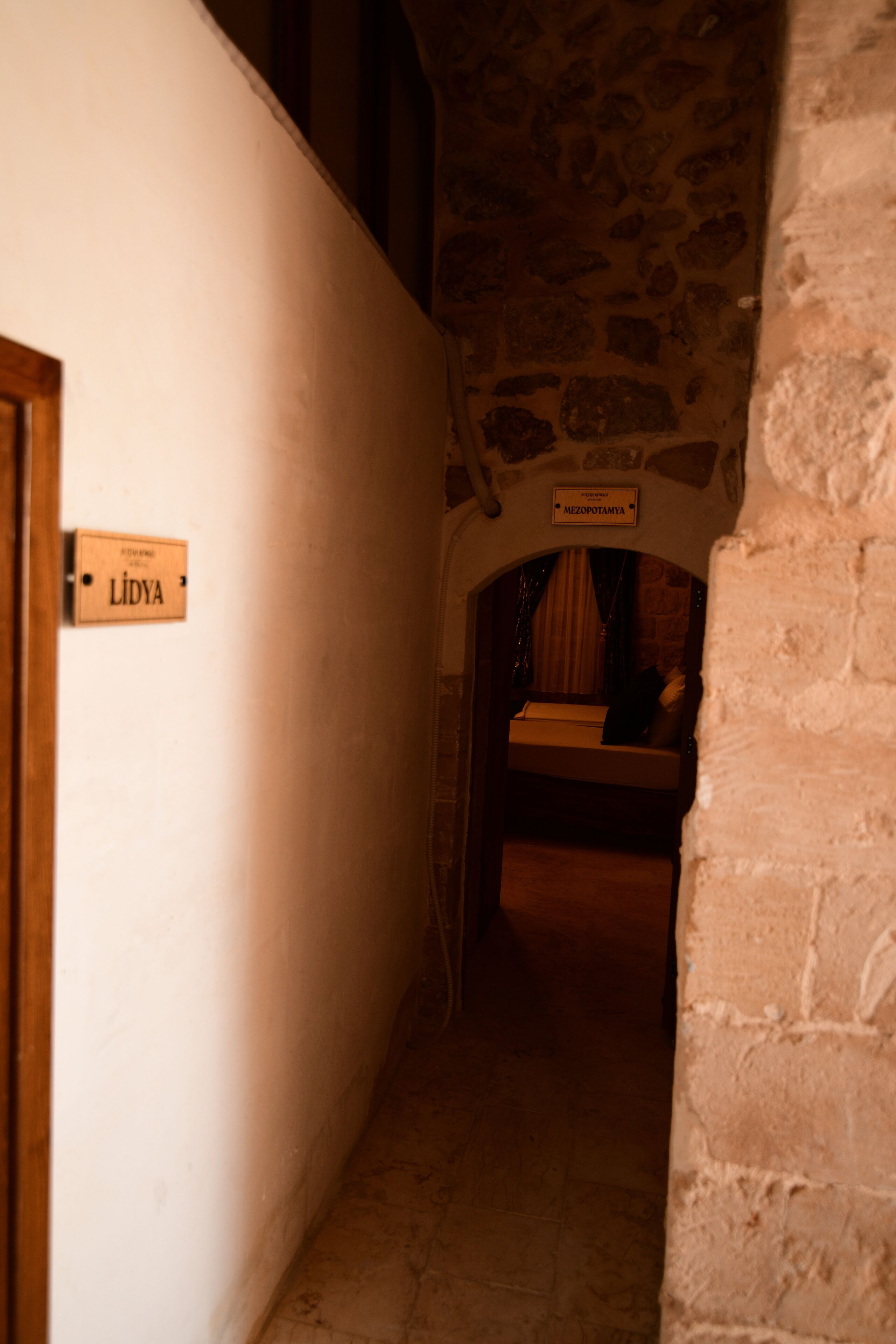 A narrow hallway with a wooden door labeled "LIDYA" and a sign above a bed reading "MEZOPOTAMYA".