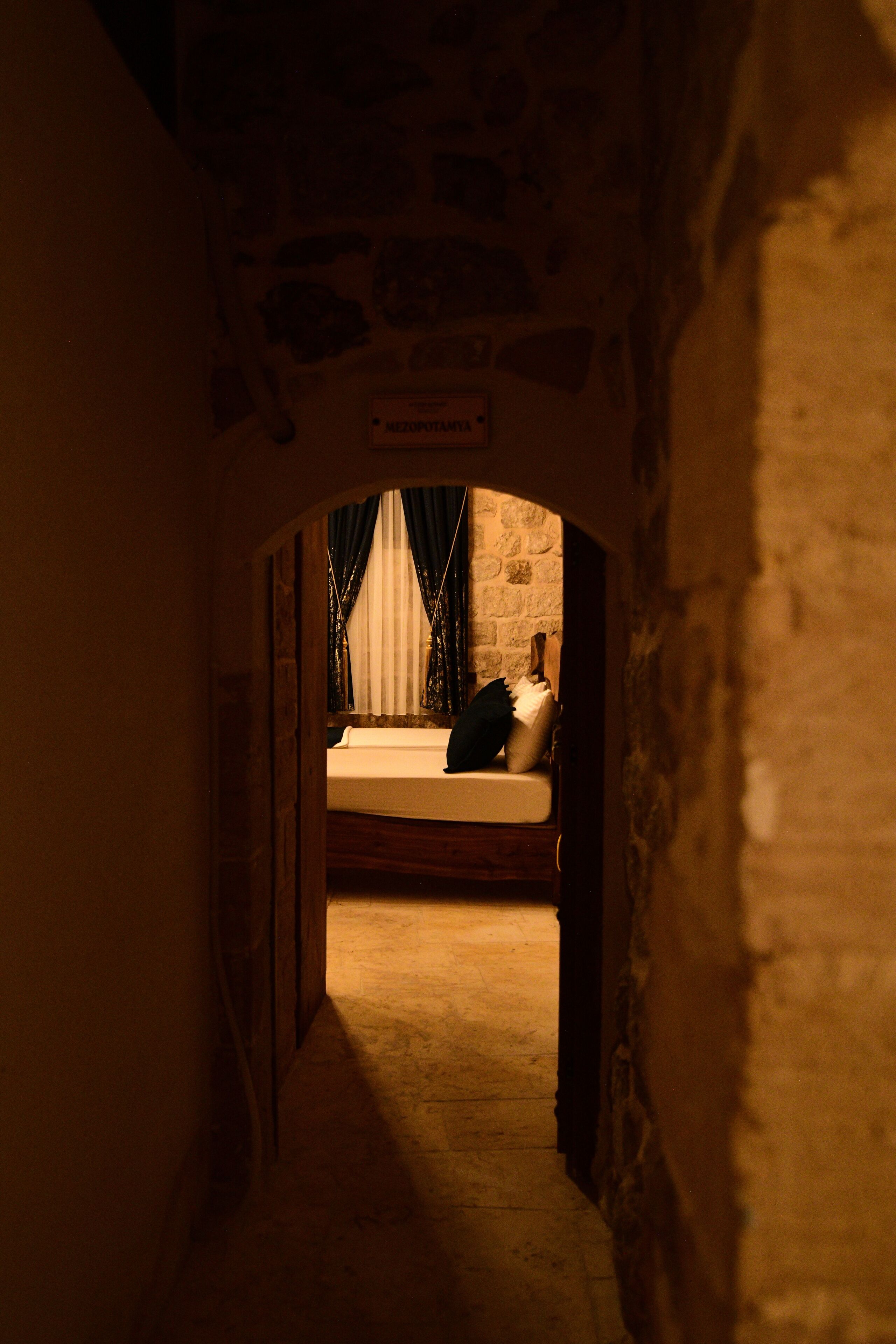 Un pasillo estrecho que conduce a un dormitorio, con una cama, un cartel sobre ella y una ventana con cortinas.