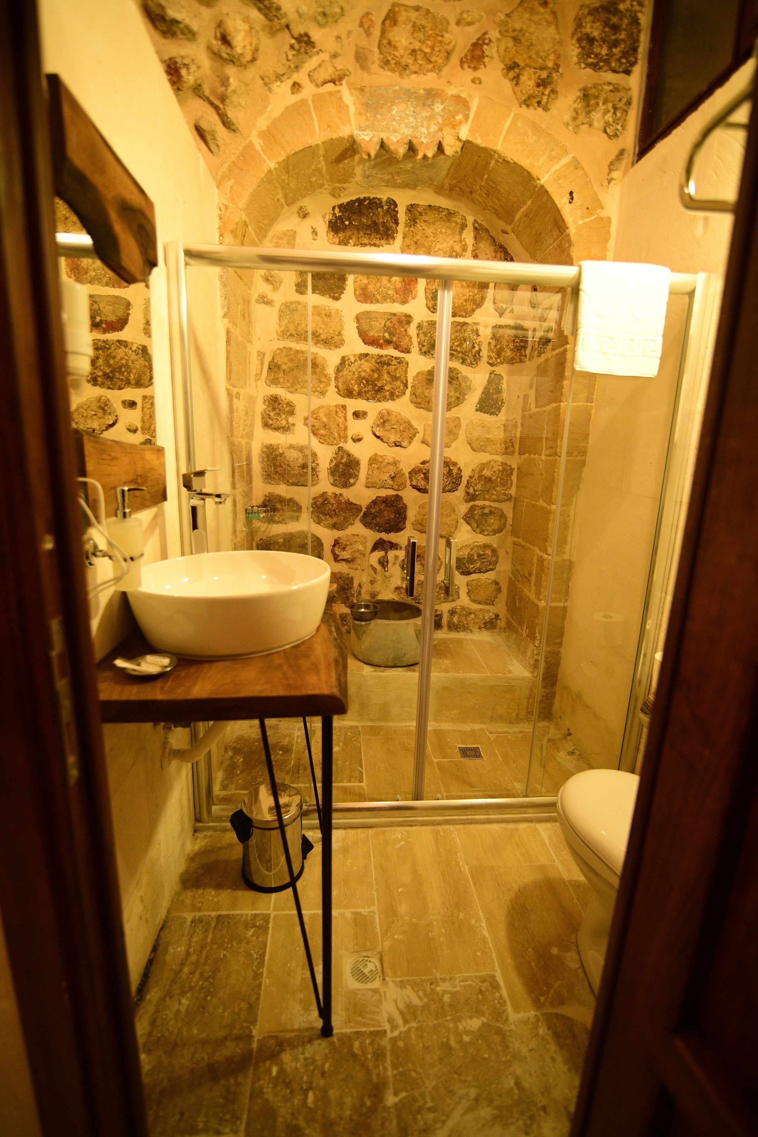 A bathroom with a stone wall, a white sink, and a glass shower enclosure.