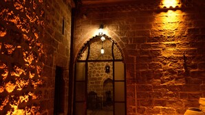 A stone-walled corridor with an arched doorway leading to a room with a bed and a nightstand. - Sultan Konagi Hotel (Mardin)