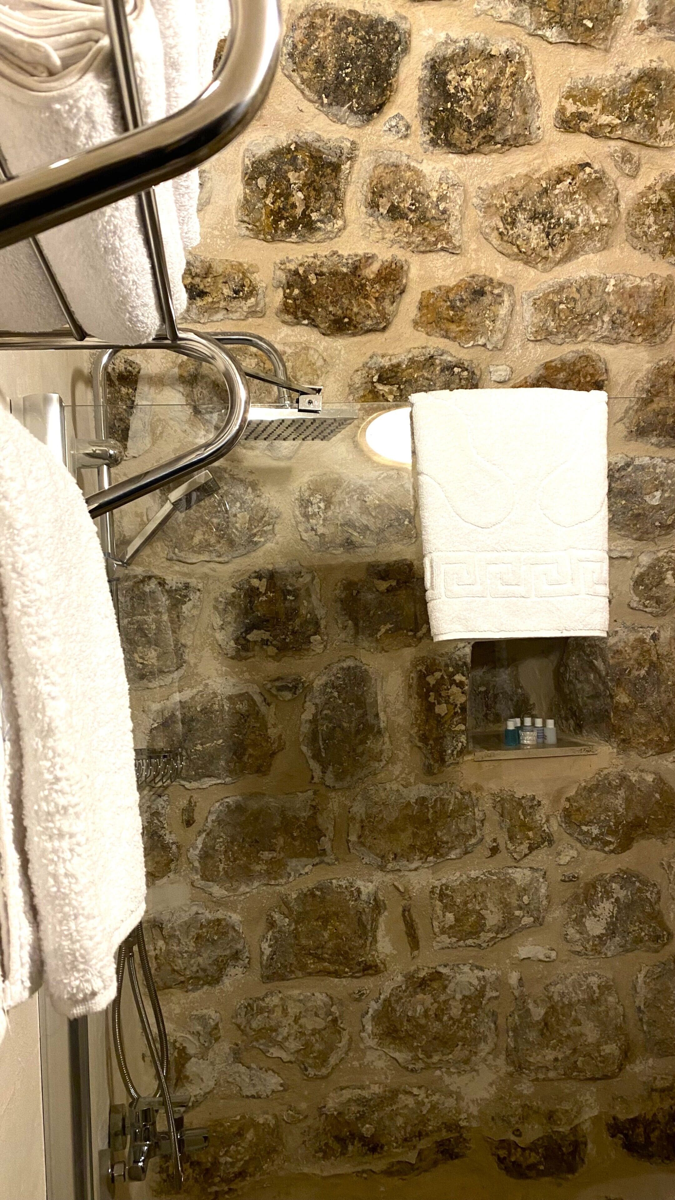 A bathroom with a stone wall, a white towel hanging on a rack, and a shower head.