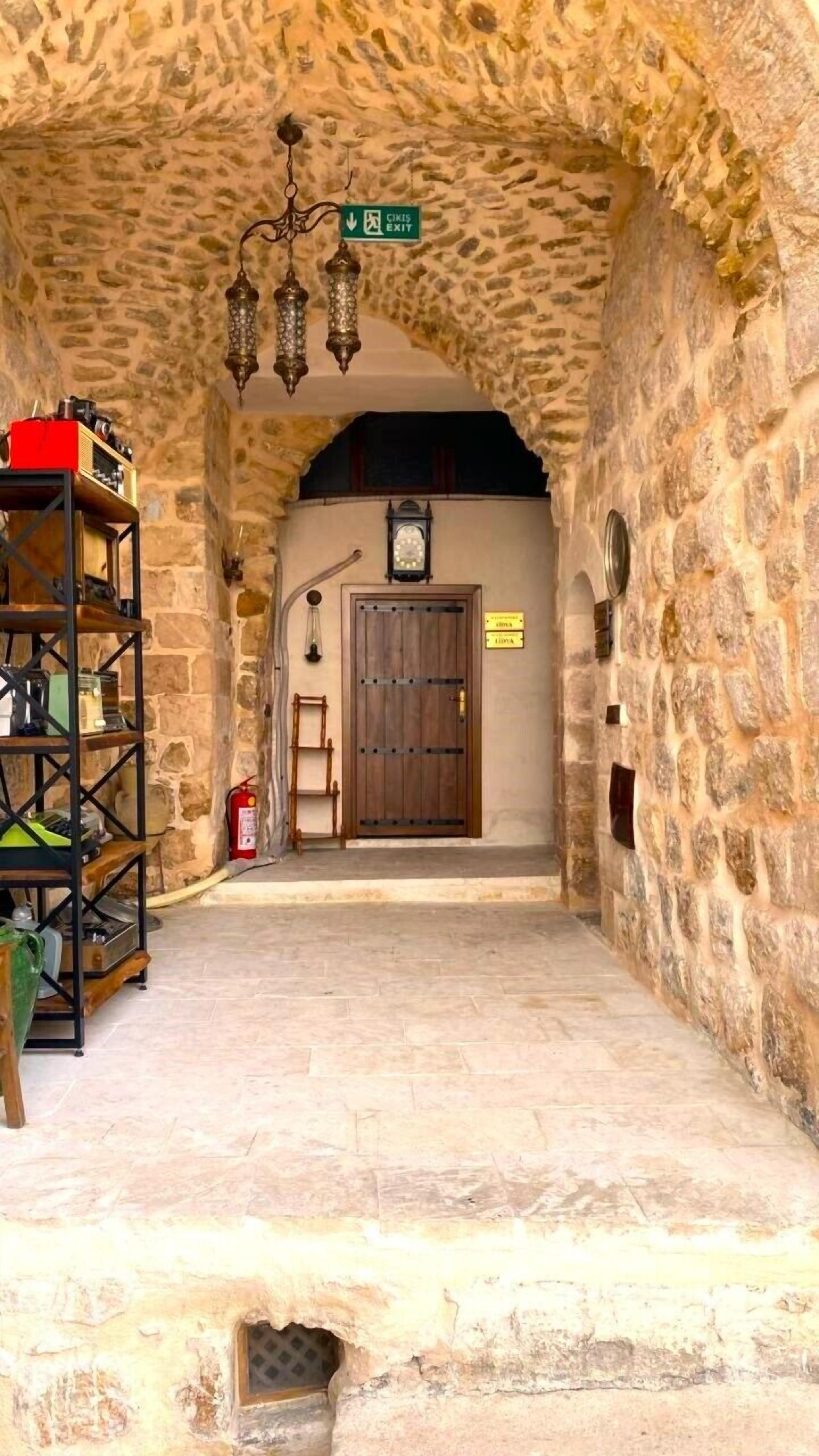 A stone-walled corridor with a wooden door, a clock, and a sign indicating an exit.