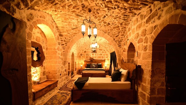 A stone-walled room with a bed, two bedside tables, and a chandelier. - Sultan Konagi Hotel (Mardin)