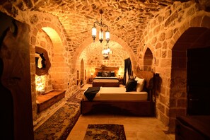 A stone-walled room with a bed, two bedside tables, and a chandelier. - Sultan Konagi Hotel (Mardin)
