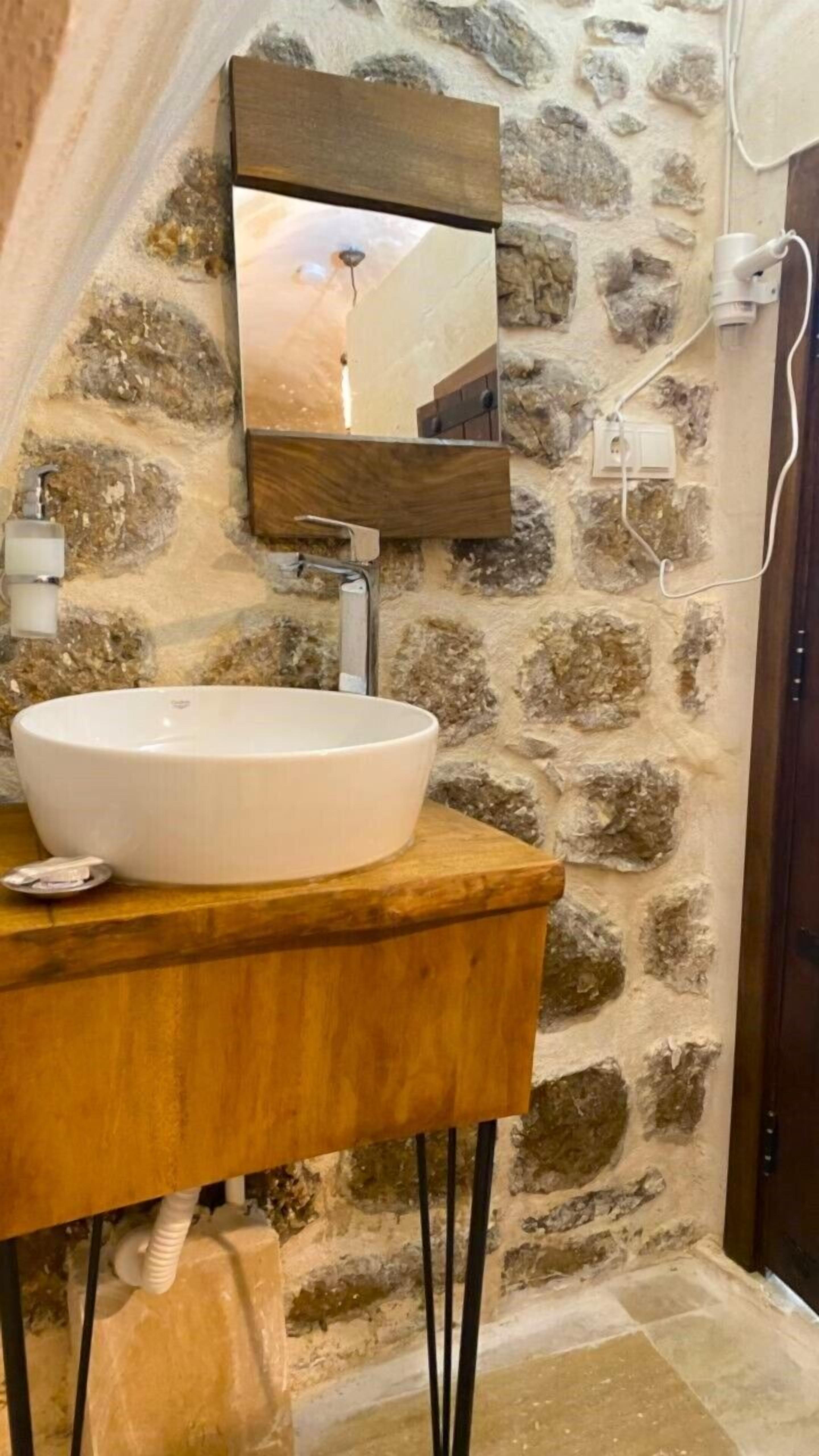 Ein Badezimmer mit Steinwand, Holzwaschtisch, weißem Waschbecken und Spiegel.