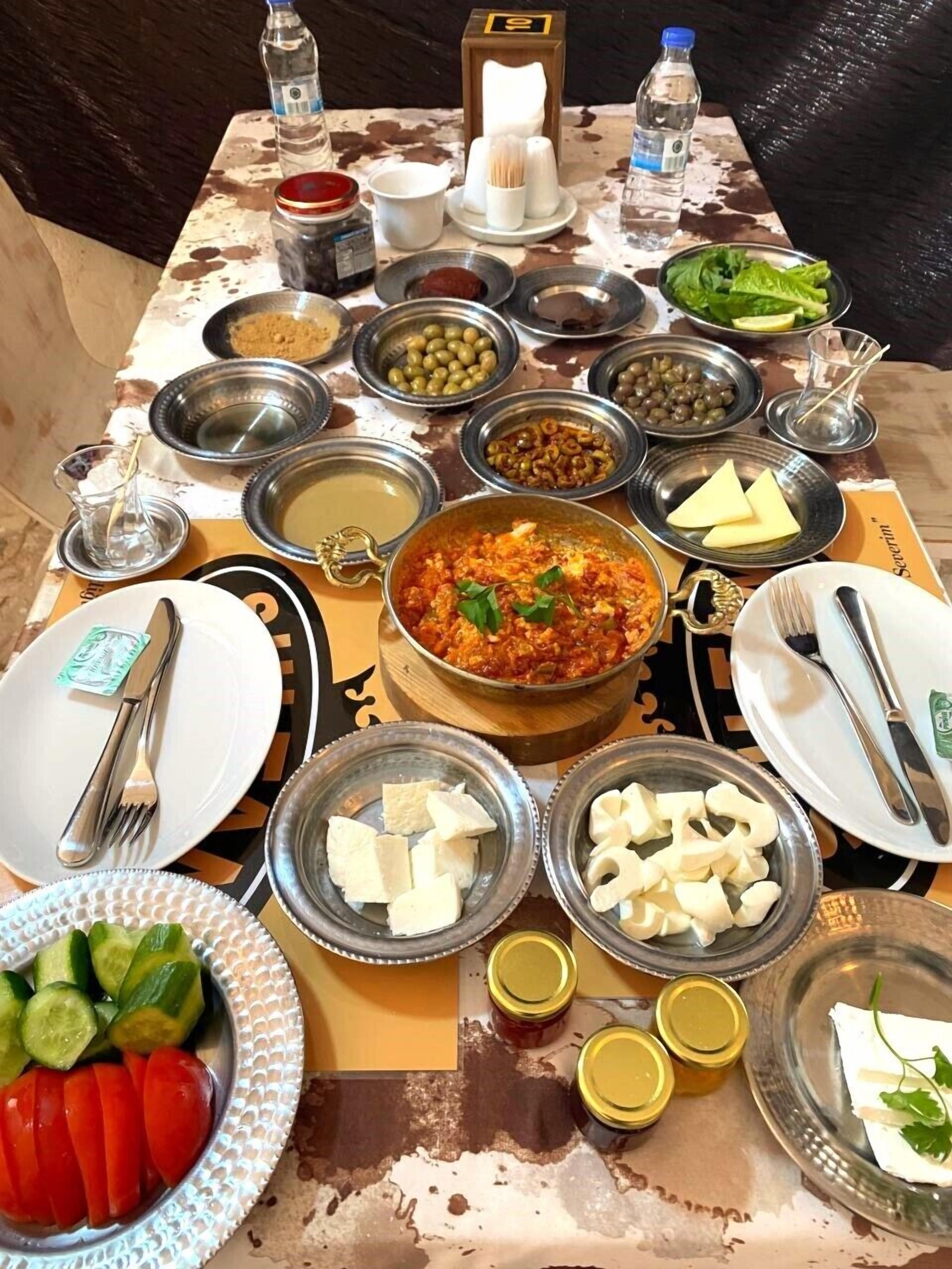 A table set with various dishes, including a central pot of stew, bowls of olives, cheese, and fresh vegetables.
