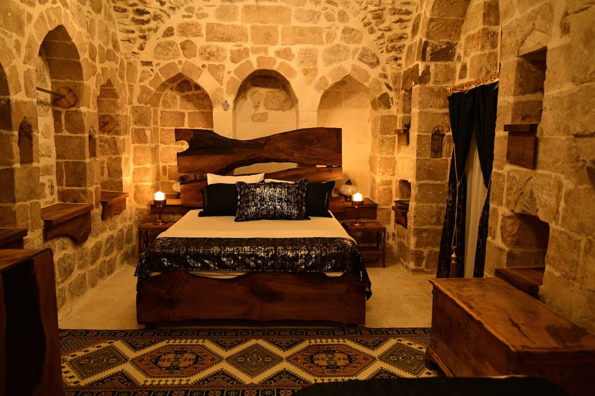 Ein Schlafzimmer mit Steinwänden, einem großen Bett, einem Holzkopfende und einem gemusterten Teppich.